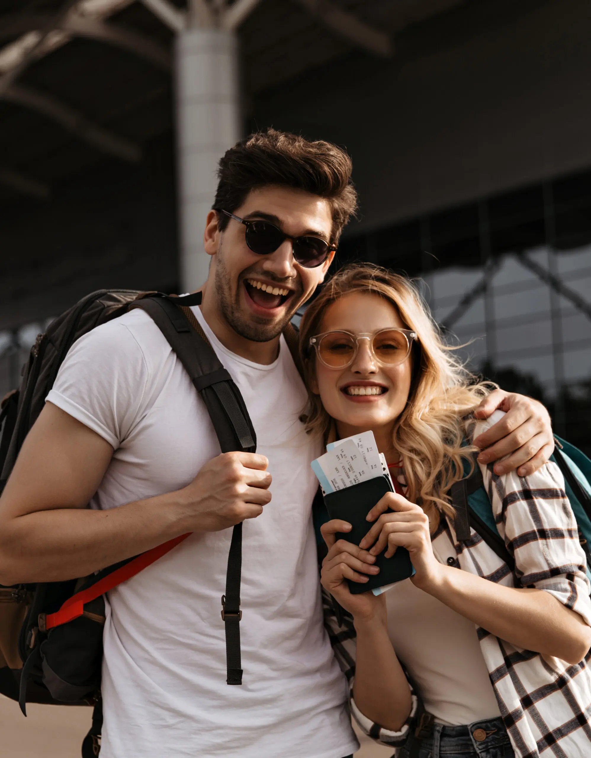 young-brunette-man-smiles-widely-hugs-his-attractive-girlfriend-couple-travelers-holds-backpacks-passports-airport-background