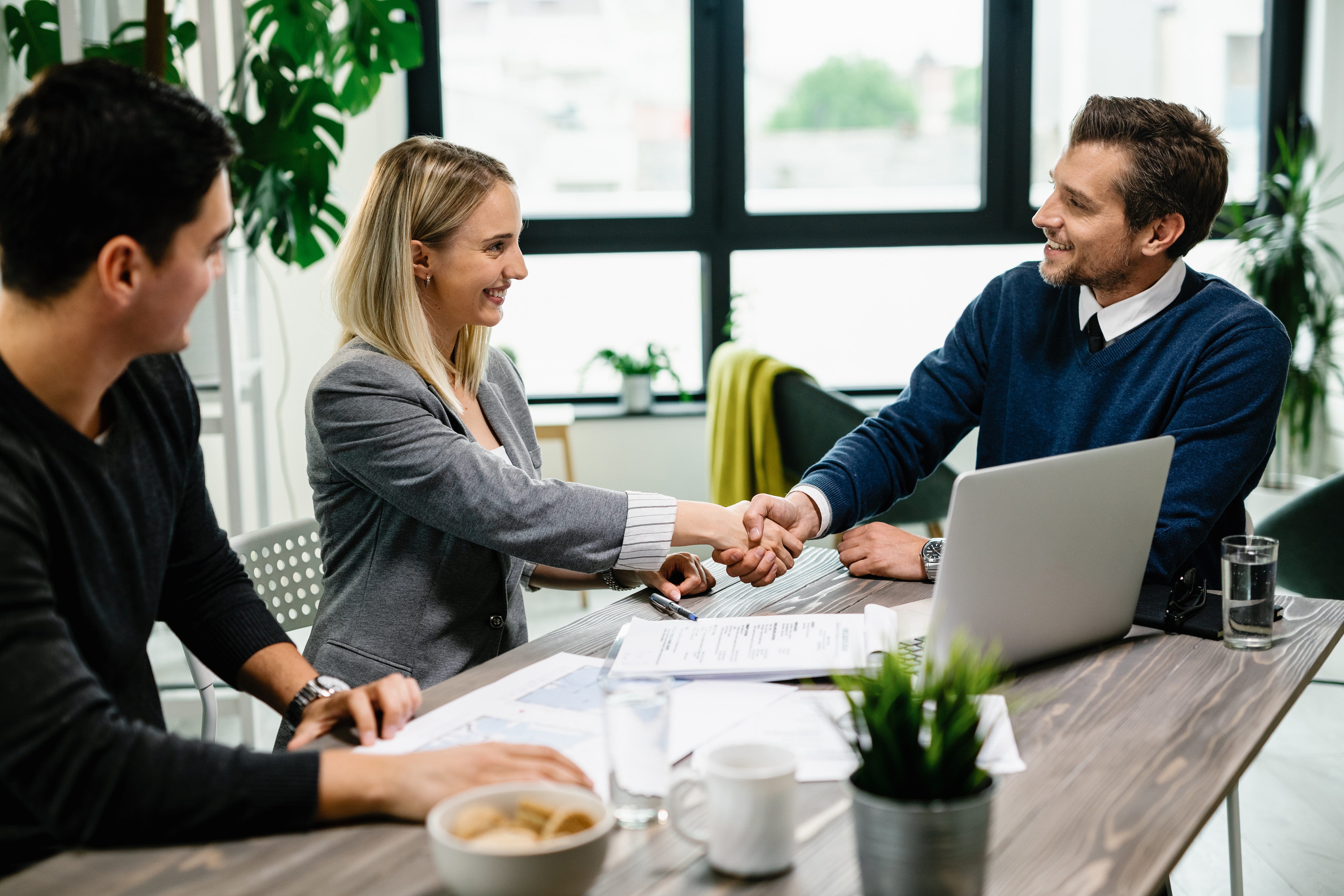Happy real estate agent greeting a young couple in the office.
